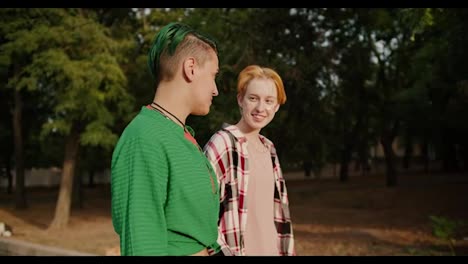 Two-girls-with-short-hair-and-bright-hair-color-in-plaid-shirts-walk,-communicate-with-each-other-and-flirt-during-their-date-in-the-park