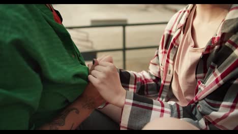 Close-up-shot-of-two-lesbian-girls-holding-hands-and-one-of-them-kissing-the-hands-of-the-other-in-the-park.-Lesbian-couple-in-the-park,-a-girl-in-a-green-shirt-and-a-girl-in-a-checkered-pink-shirt