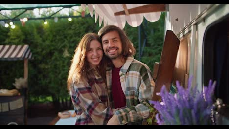 Portrait:-Happy-brunette-guy-with-his-girlfriend-in-a-plaid-shirt-hugging-and-talking-while-standing-Near-his-trailer-during-a-picnic-in-a-camp-outside-the-city-in-the-summer