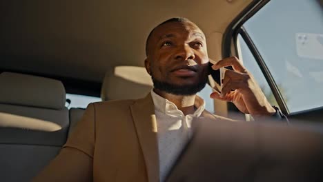 Confident-man-Businessman-with-Black-skin-color-talks-on-the-phone-and-looks-at-his-tablet-to-remember-his-plans-while-driving-in-a-modern-car-in-a-non-urban-area