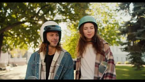 A-brunette-girl-in-a-checkered-shirt-pats-her-boyfriend-on-the-back-and-leaves-him.-A-guy-in-a-denim-shirt-with-long-and-curly-hair-in-a-white-helmet-sits-on-a-moped-and-makes-a-sad-grimace-and-smokes-a-cigarette-in-the-summer-city