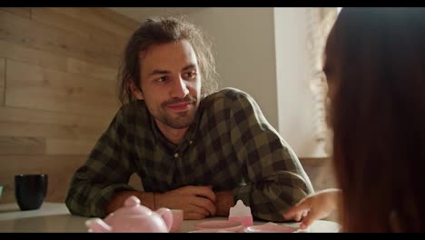 Over-the-shoulder-little-brunette-girl-in-a-pink-dress-plays-tea-party-with-the-help-of-toy-pink-cups-and-teapots-together-with-her-happy-brunette-man-father-in-a-checkered-green-shirt-in-a-modern-kitchen