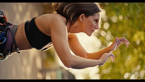 Vertical-video:-A-blonde-girl-with-a-bob-hairstyle-in-a-black-top-examines-the-climbing-wall-and-imagines-how-she-can-grab-its-ledges-with-her-hands-in-order-to-climb-up-on-a-sunny-summer-day