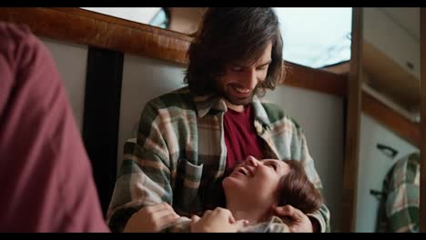 Happy-brunette-guy-in-a-green-checkered-shirt-hugs-his-brunette-girlfriend-in-pink-pants-who-lies-on-his-lap-during-their-vacation-in-a-trailer-outside-the-city-in-a-camp-during-a-picnic-in-the-summer