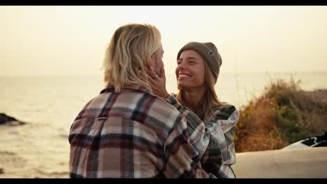 Close-up-shot-of-a-blonde-girl-in-a-Green-hat-in-a-checkered-shirt-examines-her-blond-boyfriend-and-holds-him-by-the-neck-tenderly-and-kisses-him-while-sitting-on-a-bench-on-the-sea-strawberries-during-sunrise-in-the-morning-in-summer