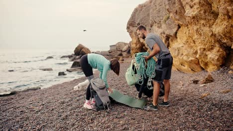 A-group-of-rock-climbers,-two-girls-and-a-brunette-guy-came-to-the-rocky-seashore-and-lay-out-their-backpacks-in-order-to-put-on-climbing-equipment-near-the-yellow-rocks-on-the-sea-during-the-day