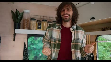 Portrait-of-a-Happy-guy-with-stubble-in-a-Green-checkered-shirt-who-dances-and-has-fun-in-his-motorhome-or-trailer-outside-the-city-during-his-vacation-and-picnic-in-the-summer