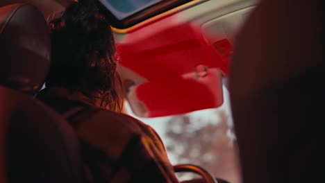 Rear-view-of-a-brunette-man-with-long-hair-in-a-checkered-shirt-driving-a-car-in-the-evening-through-the-city-after-his-work-when-he-goes-home.-Evening-ride-around-the-city