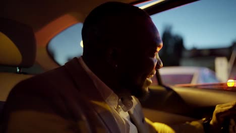 A-happy-and-cheerful-Black-skinned-man-with-a-beard-and-a-brown-suit-businessman-gets-out-of-his-modern-car-and-heads-to-a-meeting-place-in-the-city-in-the-evening