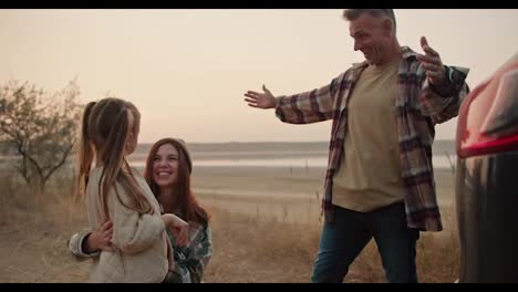 Happy-brunette-girl-hugs-with-her-little-daughter-and-middle-aged-husband-while-they-come-for-a-picnic-in-the-summer