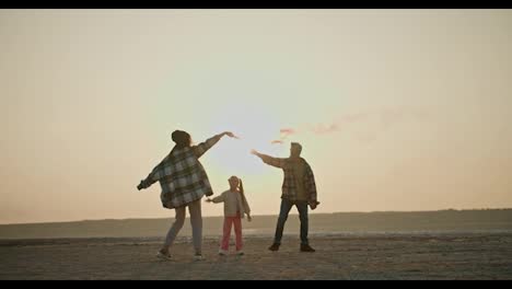 Happy-family-middle-aged-man-with-his-wife-and-little-daughter-playing-with-fireworks-that-emit-green-and-red-smoke-while-relaxing-with-a-pet-cream-colored-dog-outside-the-city-on-an-empty-deserted-seashore-in-the-summer-evening