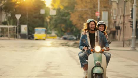 Happy-guy-with-long-curly-hair-in-a-denim-shirt-rides-with-his-happy-girlfriend-in-a-White-helmet-on-a-motorcycle-with-headlights-on-at-Sunrise-on-a-sunny-summer-morning