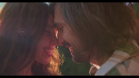 Close-up-shot-of-a-happy-couple,-a-guy-and-a-brunette-girl-rub-their-noses-against-each-other-and-communicate-during-their-picnic-outside-the-city-in-the-summer-near-the-trailer