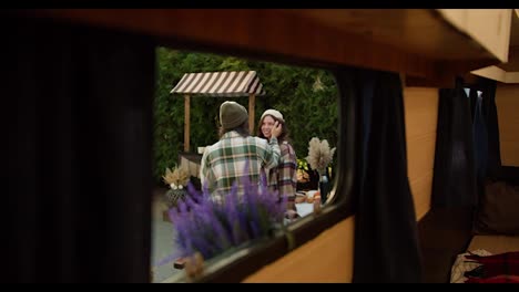 Shooting-in-a-trailer,-a-brunette-man-in-a-green-checkered-shirt-strokes-his-brunette-girlfriend-on-the-cheek-and-communicates-with-her-during-his-picnic-at-a-camp-outside-the-city-in-the-summer