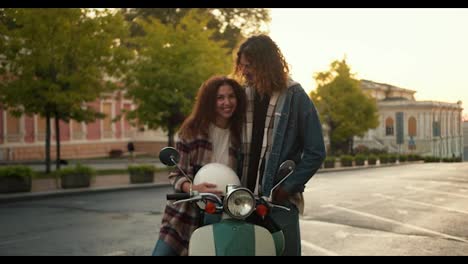 Portrait:-happy-guy-and-girl-in-plaid-shirts-with-curly-curly-hair-posing-and-looking-at-camera-Near-their-green-moped-near-a-street-with-trees-and-ancient-architecture-on-a-wide-road