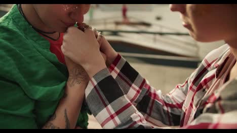 Close-up-shot-of-a-girl-in-a-green-shirt-kissing-her-girlfriends-hands-in-the-park-near-the-skate-area.-Lesbian-couple-on-a-date-in-the-park-holding-hands-and-kissing-each-other's-hands