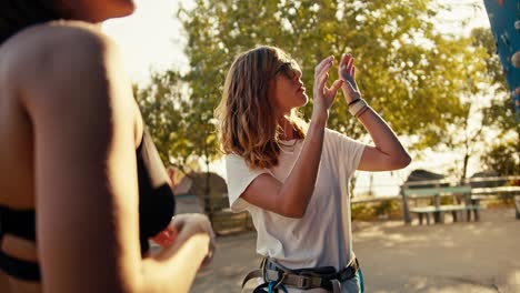 A-blonde-girl-climbing-instructor-tells-her-student-how-to-climb-up-a-blue-climbing-wall-correctly-and-shows-with-her-hands-how-to-properly-grab-the-indentations-in-the-structure.-A-blonde-girl-in-a-white-T-shirt-gives-instructions-on-rock-climbing-at-a-climbing-wall