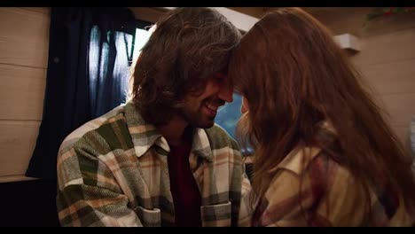 Close-up-shot-of-a-romantic-scene,-a-brunette-guy-in-a-green-checkered-shirt-rubs-his-forehead-against-his-brunette-girlfriend-in-a-checkered-shirt-while-relaxing-in-a-trailer-in-a-camp-during-a-picnic-in-the-summer