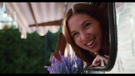 Close-up-portrait-of-a-happy-brunette-girl-sticking-her-head-out-and-looking-out-of-a-trailer-window-during-her-picnic-at-a-camp-outside-the-city-in-the-summer