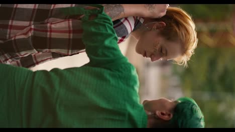 Vertical-video:-a-girl-with-green-short-hair-in-a-green-shirt-straightens-the-hair-of-her-blonde-short-haired-girlfriend-with-sparkles-on-her-face-in-a-plaid-shirt-and-chatting-with-her-during-her-date