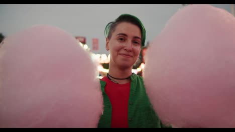 Portrait-of-a-lesbian-girl-with-a-short-green-haircut-and-sparkles-on-her-face-who-holds-two-huge-cotton-candy-in-an-amusement-park