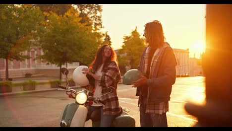 A-girl-and-a-guy,-brunettes-in-checkered-shirts,-take-off-their-protective-helmets-for-riding-a-moped,-hug-and-rejoice-at-Sunrise-on-the-street.-Happy-couple-guy-and-girl-take-off-their-protective-helmets,-straighten-their-hair-and-communicate