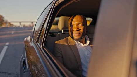 A-confident-man-with-Black-skin-opens-the-rear-window-in-a-modern-car-and-looks-out-of-it-during-his-trip-and-business-trip-outside-the-city