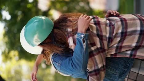 Vertical-video-of-a-happy-brunette-guy-with-curly-hair-in-a-moped-helmet-hugs-his-brunette-girlfriend-in-a-checkered-shirt-in-a-beautiful-summer-city