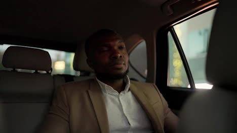 A-happy-and-confident-man-with-Black-skin-and-a-beard-in-a-brown-suit-rides-in-a-modern-car-after-a-business-meeting-and-looks-out-the-window