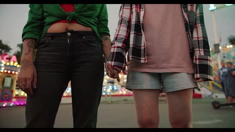 Close-up-shot-of-a-girl-in-a-checkered-pink-shirt-and-a-girl-in-a-green-shirt-holding-hands-and-bringing-their-heads-together-and-rubbing-their-foreheads-together-during-their-warm-date-in-the-amusement-park