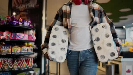 Close-up-shot-of-a-man-in-a-plaid-shirt-with-Black-skin-color-carrying-huge-packages-of-disposable-white-towels-and-walking-along-counters-with-vegetables-and-fruits-in-a-modern-grocery-store