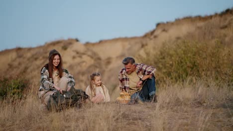 Un-Hombre-De-Mediana-Edad-Con-Una-Camisa-A-Cuadros-Junto-Con-Su-Esposa,-Una-Chica-Morena-Con-Una-Camisa-A-Cuadros-Verde,-Se-Relajan-Durante-Su-Picnic-Fuera-De-La-Ciudad-Y-Sacan-Un-Termo-Para-Beber-Té-En-Una-Tarde-De-Verano.