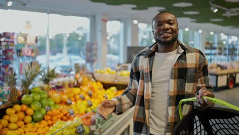 Portrait-of-a-Happy-man-with-Black-skin-color-in-a-plaid-shirt-and-a-white-T-shirt-who-is-happy-and-dancing-in-a-grocery-store-holding-a-grocery-basket-in-his-hands