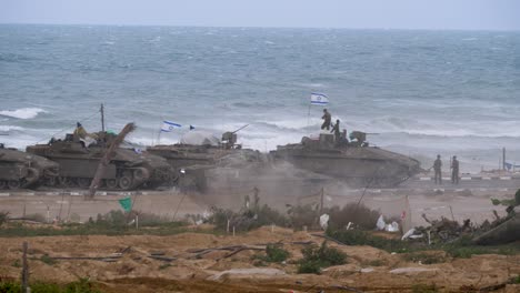 Israeli-tank-driving-past-parked-tanks-on-the-beach,-Gaza-conflict