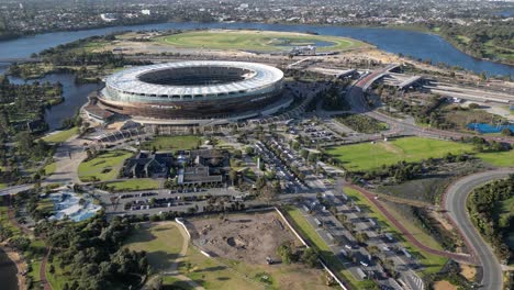 Aerial-approaching-shot-of-road-with-cars-at-Optus-Stadium-with-Swan-River-during-sunset-time---Panorama-wide-shot