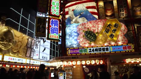 Pan-Right-Shot-Across-Illuminated-Colourful-Display-Above-Restaurant-With-Biliken-Statue-On-Corner-In-Shinsekai-Area-At-Night