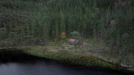 -Hildremsvatnet,-Trondelag-County,-Norway---A-Calm-Lake-Enveloped-by-a-Grove-of-Trees,-With-a-Fisherman's-Cottage-Nestled-Along-the-Lakeshore---Aerial-Pullback