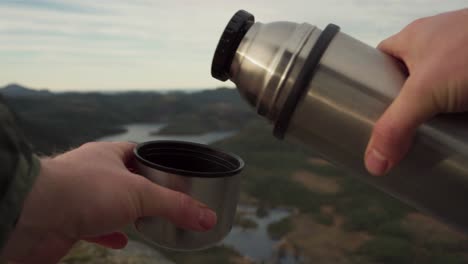 A-Closeup-Shot-of-a-Hand-Carefully-Pouring-Coffee-From-a-Stainless-Steel-Tumbler-in-Hildremsvatnet,-Trondelag-County,-Norway