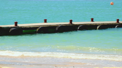 Low-jetty-with-bollards-juts-into-clear-blue-ocean-with-lapping-waves,-tranquil