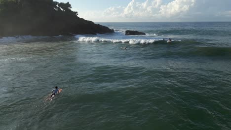 Pullback-Aerial-Drone-Shot-of-Male-Surfer-Sitting-on-Surfboard-and-Riding-a-Wave-out-towards-Sea-in-Southern-Sri-Lanka