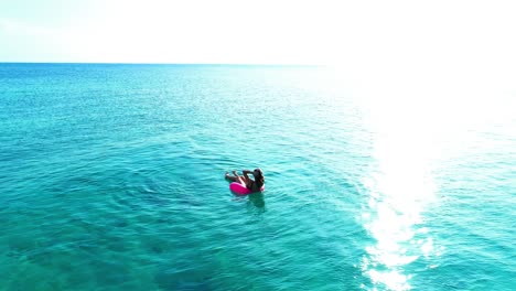 Woman-relaxes-floating-in-ocean-in-pink-tube-floatie-in-crystal-clear-blue-caribbean-water