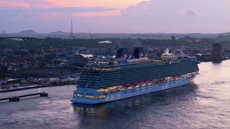 Side-angle-view-of-cruise-liner-docked-at-Caribbean-port-with-town-in-view-behind,-aerial-rising
