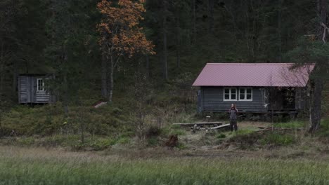 Ein-Mann-Steht-In-Der-Nähe-Eines-Holzhauses-Auf-Waldbergen-In-Hildremsvatnet,-Norwegen
