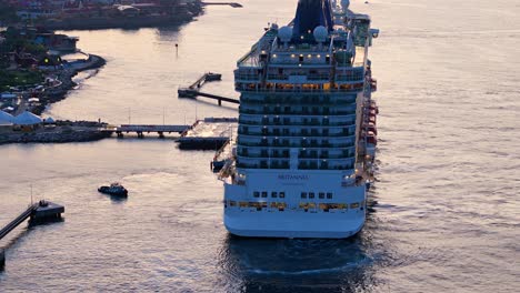 Rear-orbital-view-around-cruise-ship-at-sunset,-lights-illuminate-bedroom-and-walkways,-aerial-overview