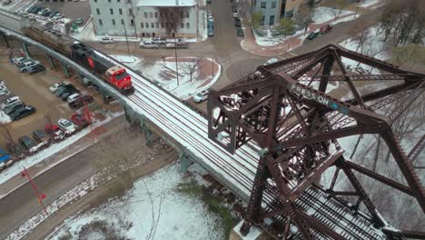 Ein-4K-Breitbild-Drohnenclip-Einer-Großen-CN-Eisenbahnlokomotive-Für-Den-Industriellen-Kohletransport,-Die-Im-Winter-In-Winnipeg,-Manitoba,-Kanada,-Gleise-Durch-Eine-Stahlbrücke-über-Den-Fluss-Hinunterfährt