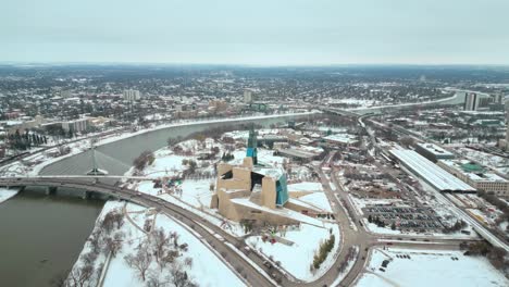 Toma-De-Establecimiento-Museo-Canadiense-De-Derechos-Humanos-Urbano-Winnipeg-Manitoba-Canadá-Centro-Rascacielos-Edificios-En-La-Ciudad-Paisaje-Nublado-Horizonte-Nevando-Invierno-Drone-4k-Disparo-Lento-Cinematográfico