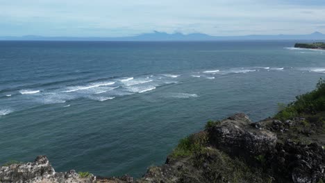 Distant-mountains-across-the-open-ocean-with-rolling-waves-and-cliffs-in-Uluwatu,-Bali,-Indonesia