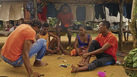 Un-Grupo-De-Jóvenes-Africanos-Jugando-Al-Juego-De-Siete-Cartas-En-La-Calle-Sobre-Una-Manta-Frente-Al-Puesto-Del-Mercado