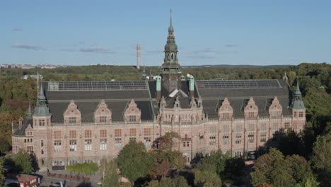 Aerial-view-of-Nordiska-Museet-with-on-sunny-evening-with-forest-and-Kaknästornet-in-background-on-Djurgården-in-Stockholm,-Sweden