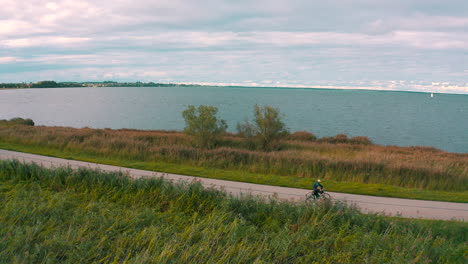 Drohne-Fliegt-In-Der-Nähe-Von-Radfahrern-Auf-Dem-Radweg-Mit-Meer-Im-Hintergrund